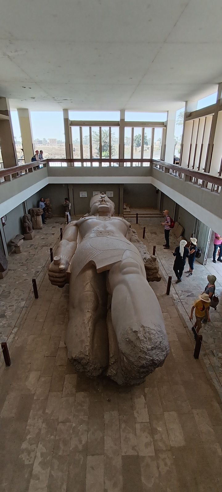 Grande statue à l'intérieur d'un musée avec des touristes qui l'observent.
