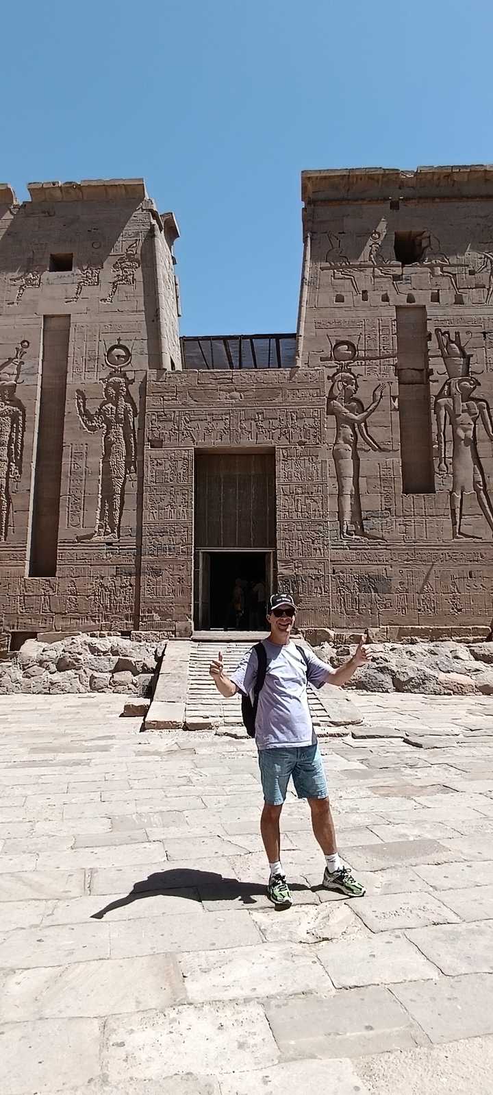 Homme posant devant un temple antique avec des reliefs.