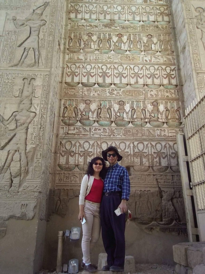 Couple posant devant des sculptures murales avec des hiéroglyphes.