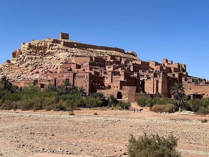 Le ksar emblématique en briques de terre d'Aït-Ben-Haddou et son édifice au sommet de la colline sous un ciel dégagé.