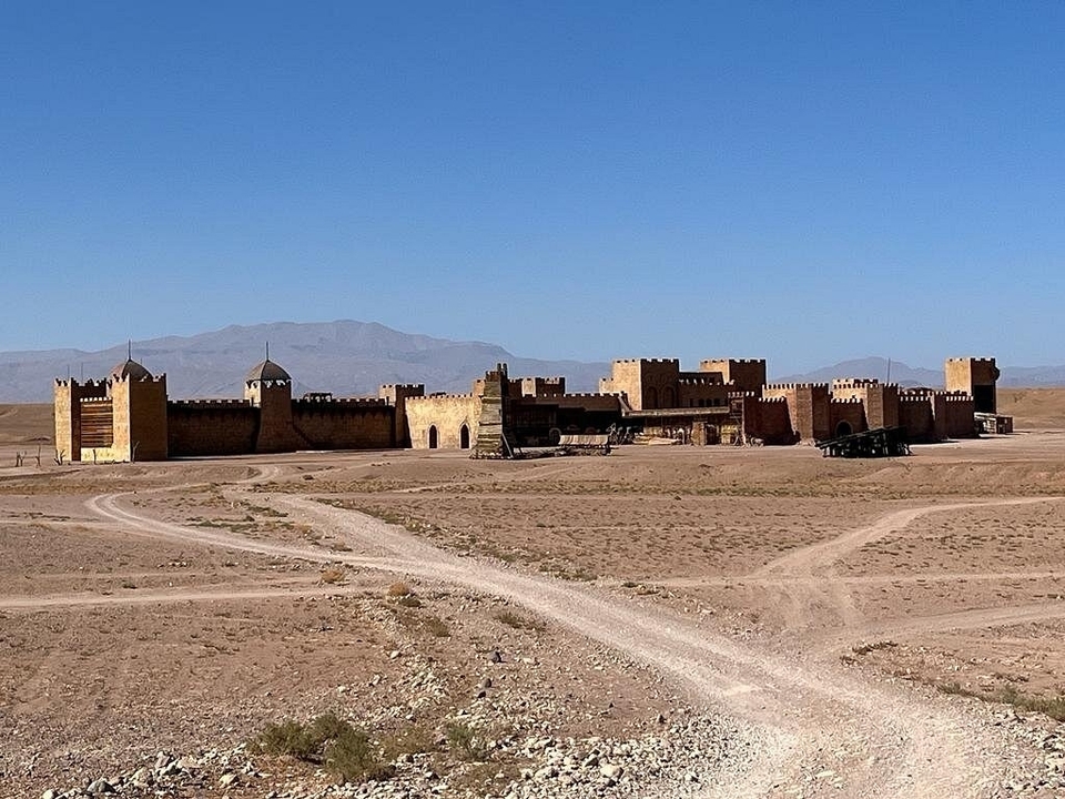 Un village médiéval fortifié dans le désert avec un paysage de montagnes en arrière-plan.