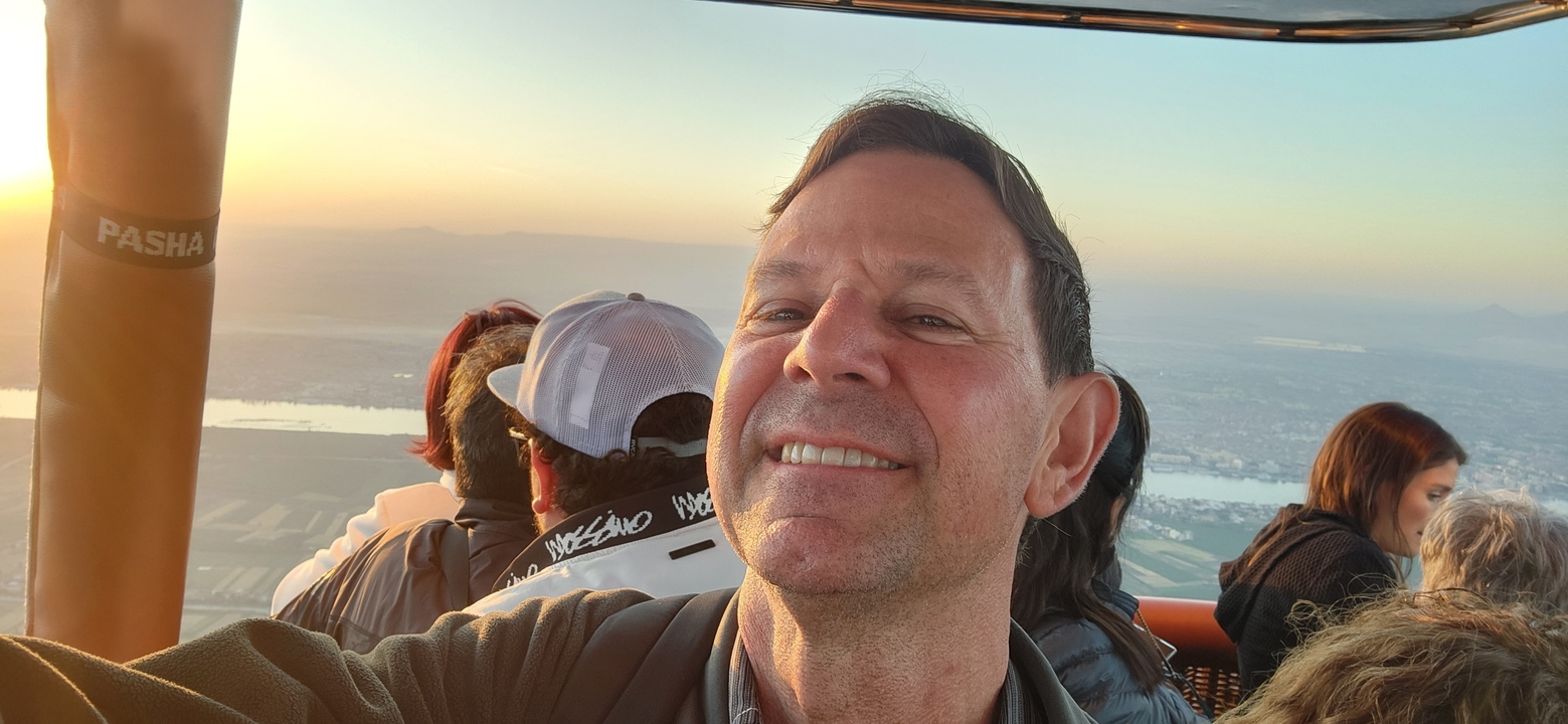 Personne prenant un selfie dans une montgolfière avec le paysage en contrebas.