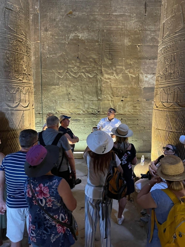 Groupe de touristes écoutant un guide parmi des colonnes antiques.