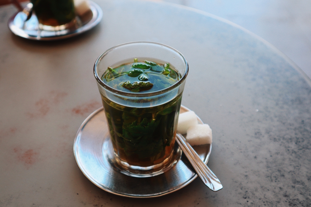 Un verre de thé à la menthe avec des morceaux de sucre sur une soucoupe.