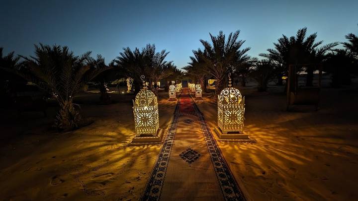 Sentier avec des lanternes allumées menant à travers les palmiers au crépuscule.