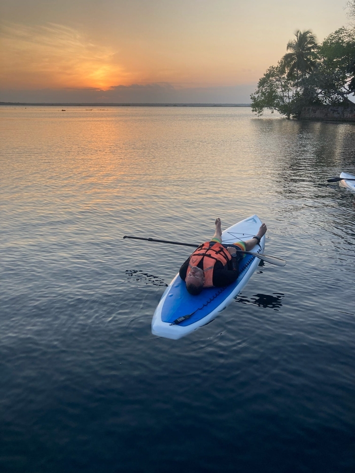 Personne sur un kayak se relaxant sur une eau calme pendant le coucher du soleil.