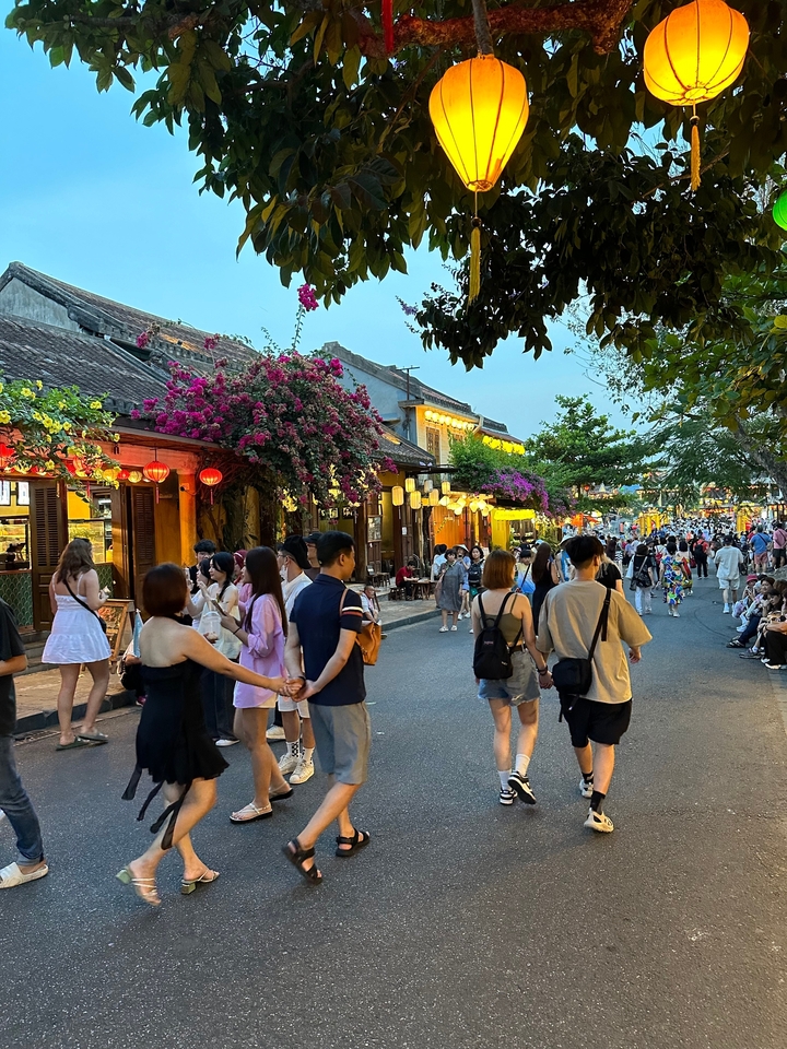 Scène de rue animée avec des touristes et des lanternes traditionnelles dans un marché.