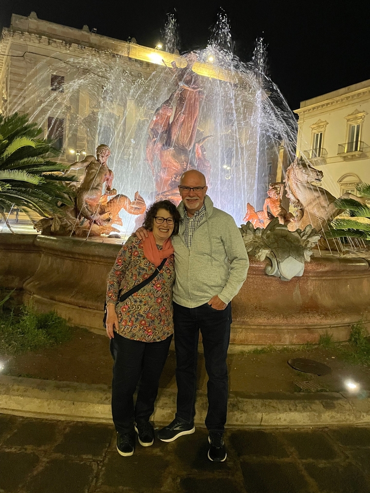 Couple posant la nuit devant une fontaine éclairée.