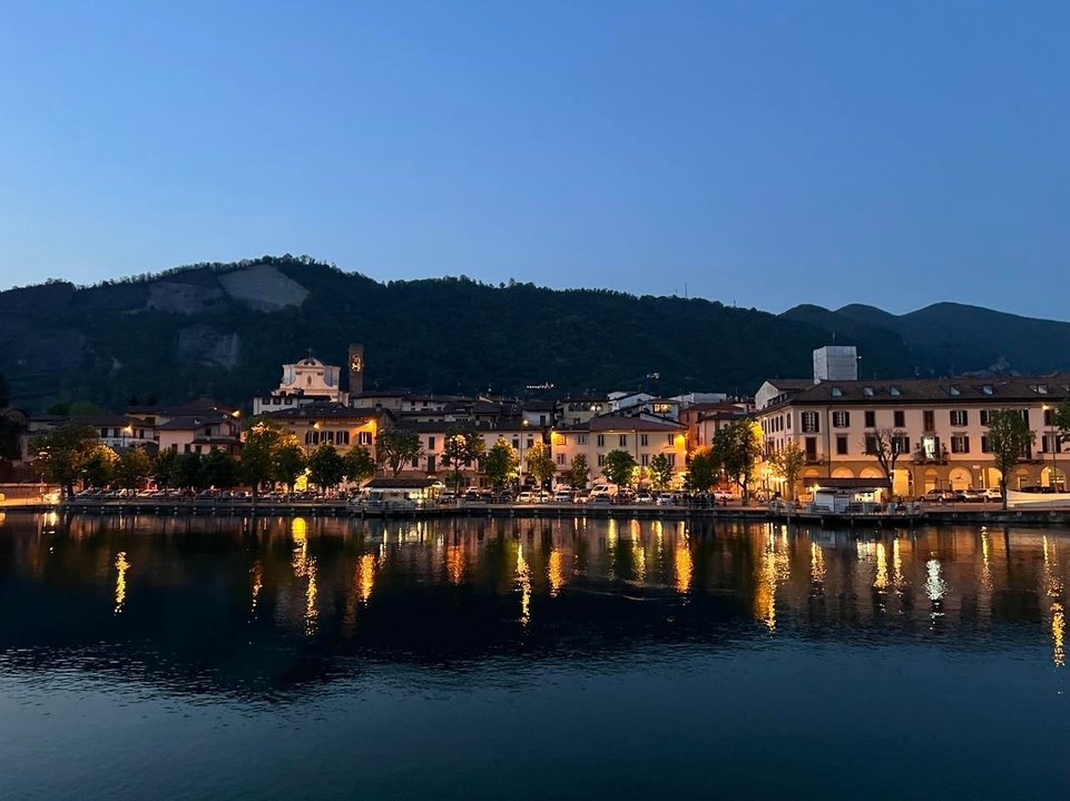 Vue du soir d'une ville au bord de l'eau avec des reflets et des silhouettes de montagnes.