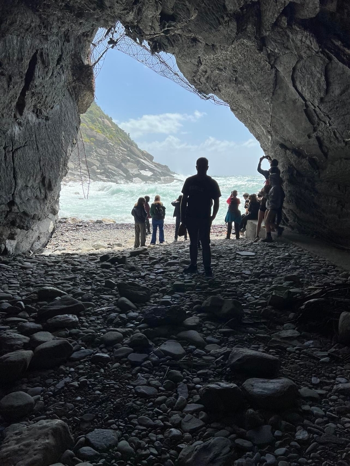 Des gens debout à l'entrée d'une grotte avec vue sur la mer.