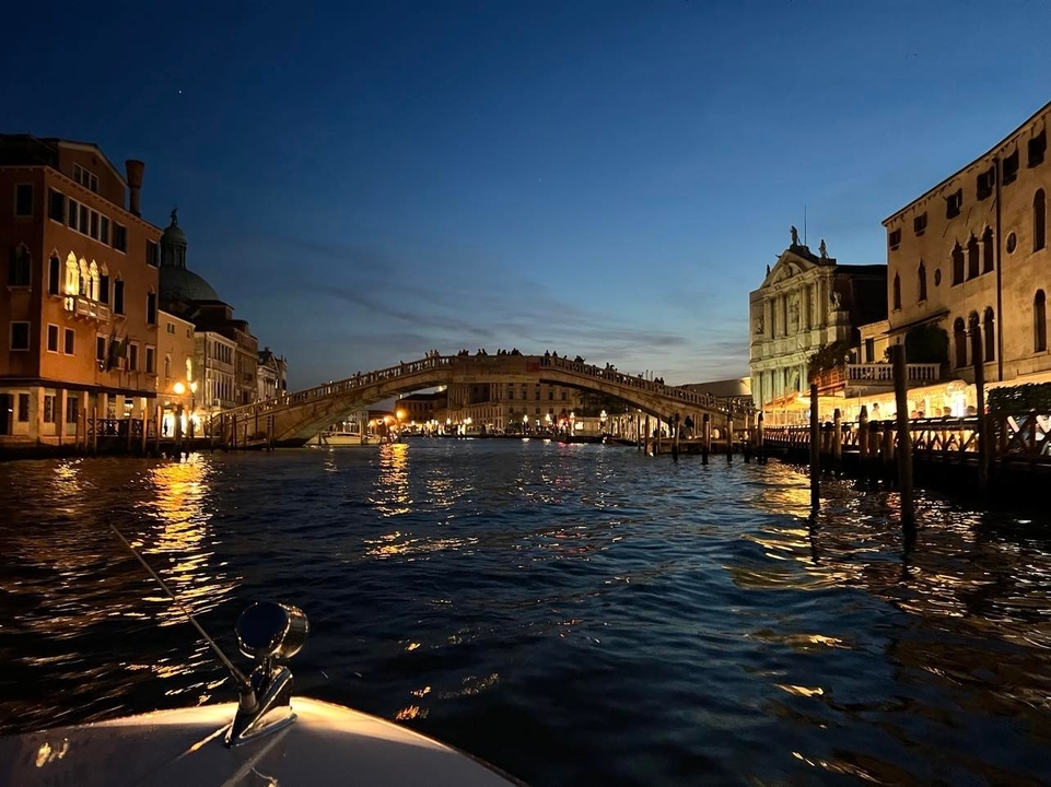 Un célèbre pont au-dessus d'un canal à Venise la nuit avec des lumières qui se reflètent sur l'eau.