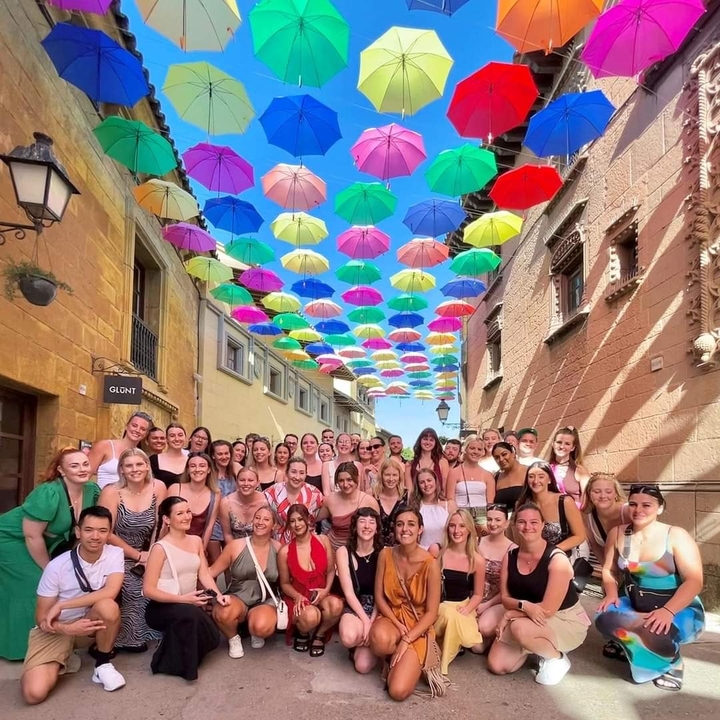 Grand groupe de personnes posant sous des parapluies colorés dans une rue.