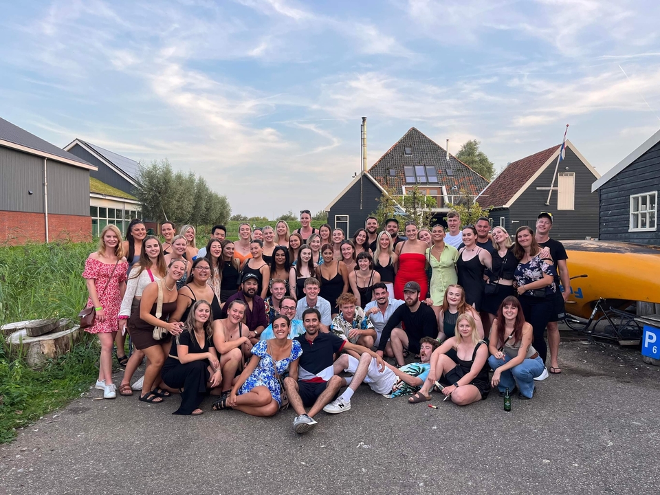 Un grand groupe de personnes posant à l'extérieur avec des maisons traditionnelles néerlandaises en arrière-plan.