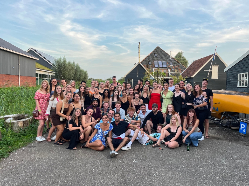 Un grand groupe de personnes posant en extérieur avec des maisons traditionnelles hollandaises.