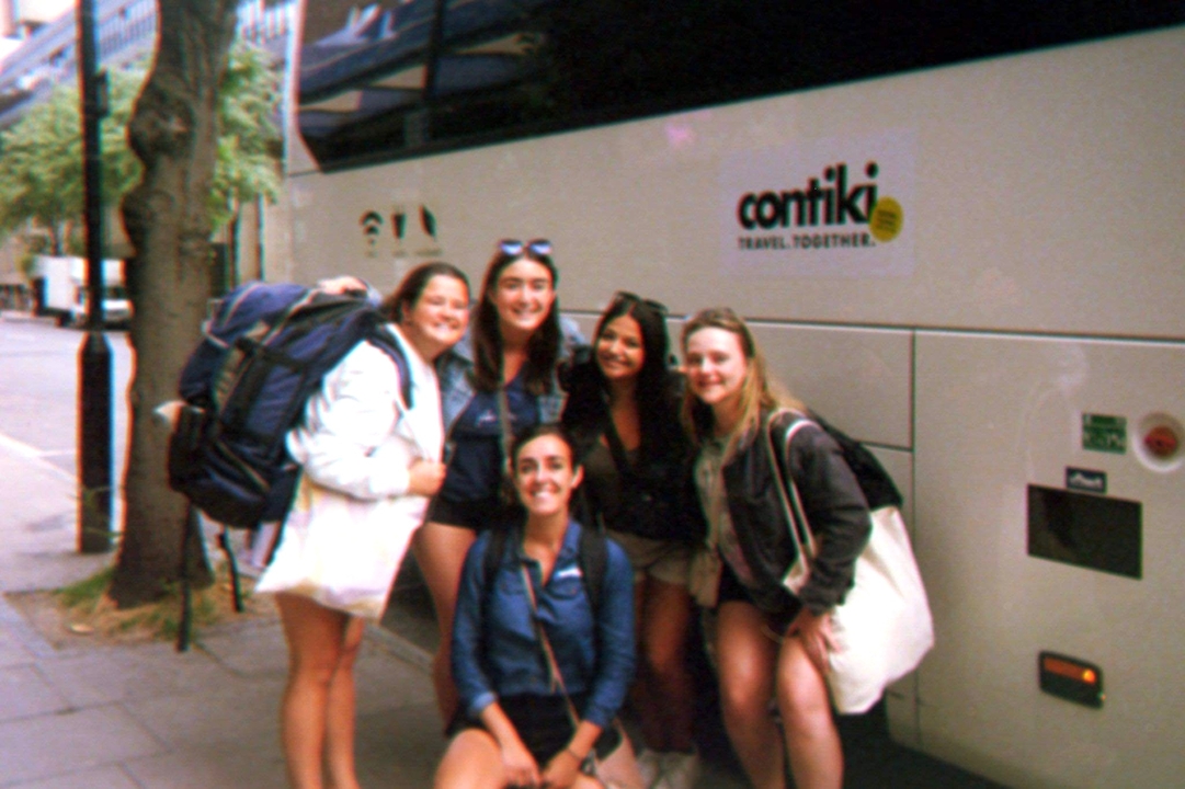 Cinq amis prenant la pose avec des sacs à dos à côté d'un bus de voyage.