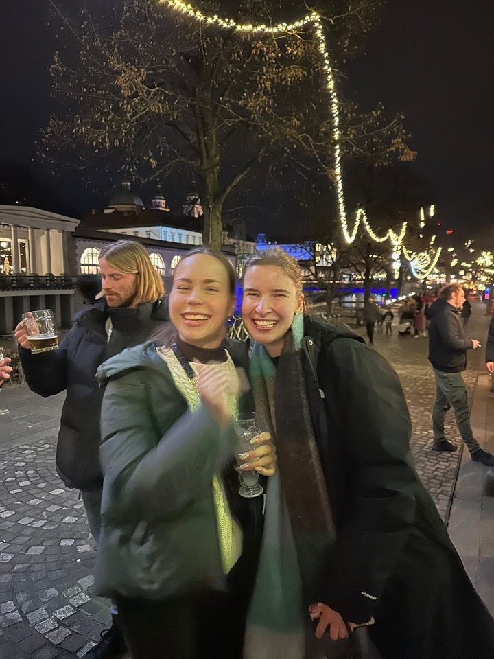 Deux femmes souriantes à l'extérieur avec des décorations illuminées derrière elles.