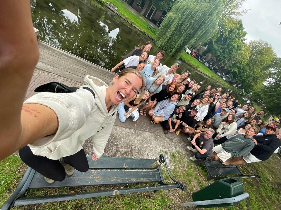 Grand groupe posant près d'un canal, une personne au premier plan prenant un selfie.