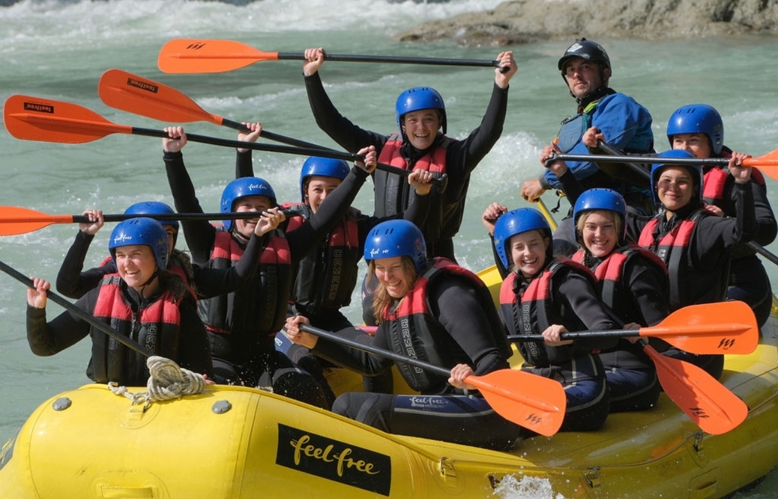 Des personnes dans un radeau avec des pagaies sur une rivière, portant des casques et des gilets de sécurité.