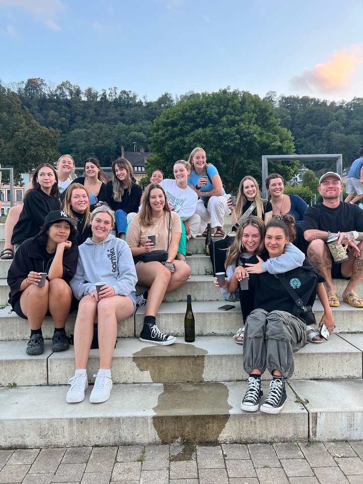 Un groupe de personnes assises sur des escaliers à l'extérieur, certaines tenant des boissons et une bouteille de vin visible.