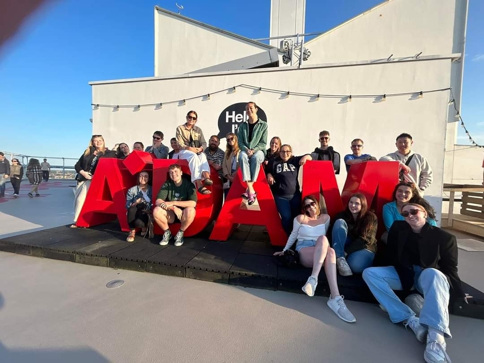 Un groupe de personnes assises sur de grandes lettres rouges A'DAM.