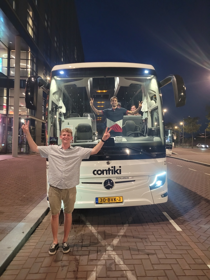 Des gens posant avec un autocar de tourisme portant l'inscription « contiki » la nuit.