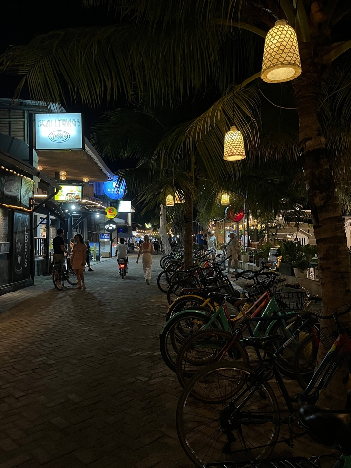 Scène de vie nocturne animée avec des gens, des vélos et des boutiques éclairées.