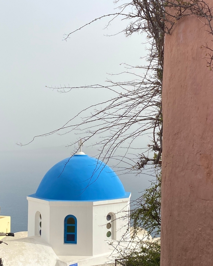 Une église avec un dôme bleu et un arbre, sur un arrière-plan brumeux.