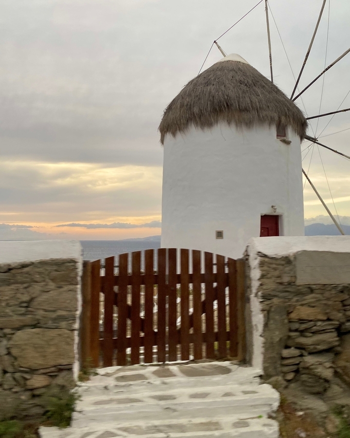 Un moulin à vent blanc au coucher du soleil avec des murs de pierre au premier plan.