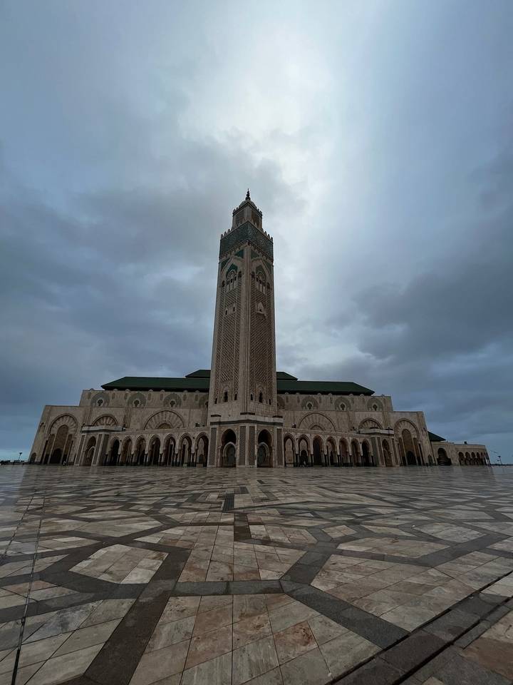 Grande mosquée avec haut minaret et arches complexes sous un ciel nuageux.