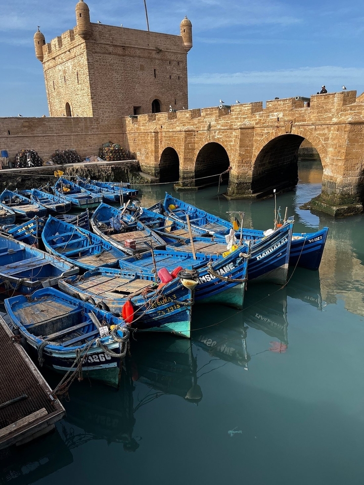 Bateaux de pêche bleus amarrés près d'un pont en arc de pierre.