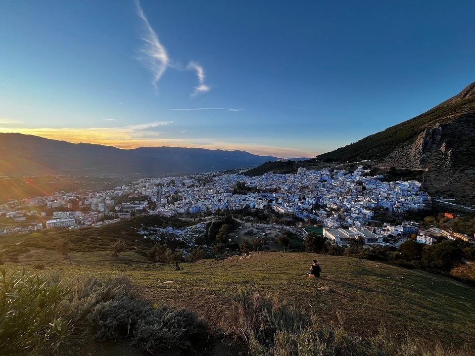 Vue depuis une colline d'une ville bleue avec un coucher de soleil en arrière-plan.