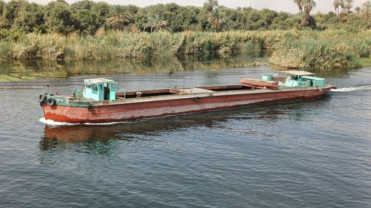 Péniche naviguant sur une rivière entourée de végétation.