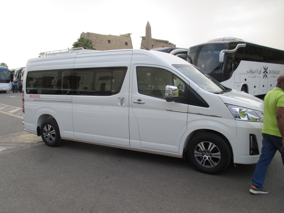 Camionnette blanche garée parmi les bus avec une personne à proximité.