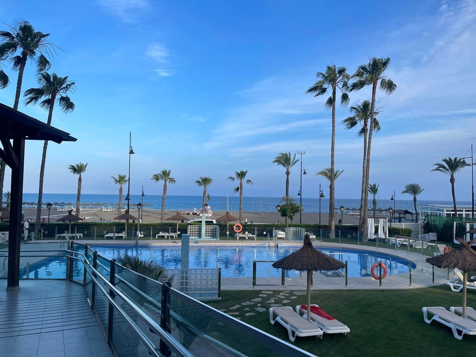 Zone de piscine du complexe hôtelier avec palmiers donnant sur la mer.