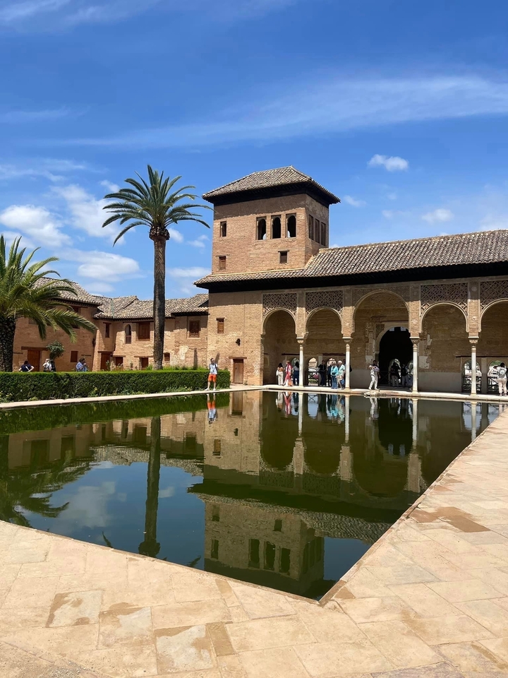 Des personnes visitant un palais mauresque historique avec un bassin de réflexion.