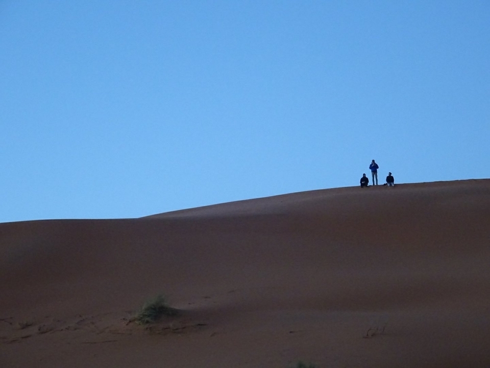 Des silhouettes lointaines se dressant sur une dune de sable.
