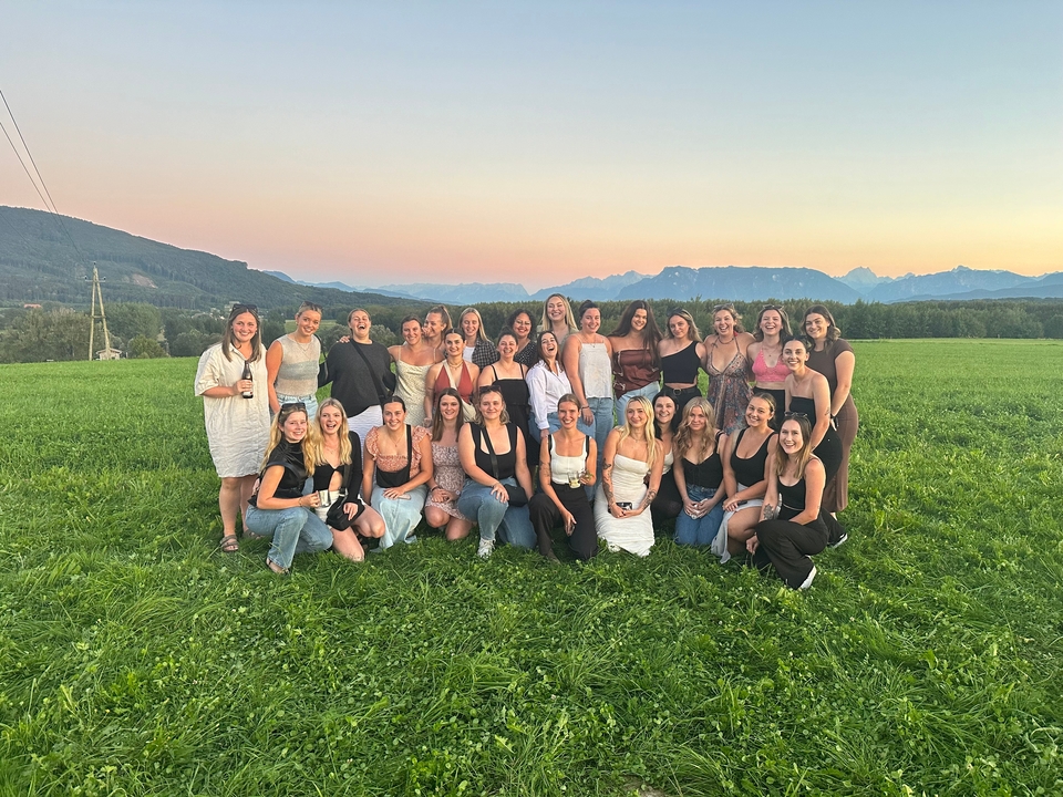 Un grand groupe de personnes posant dans un champ avec des montagnes au coucher du soleil.