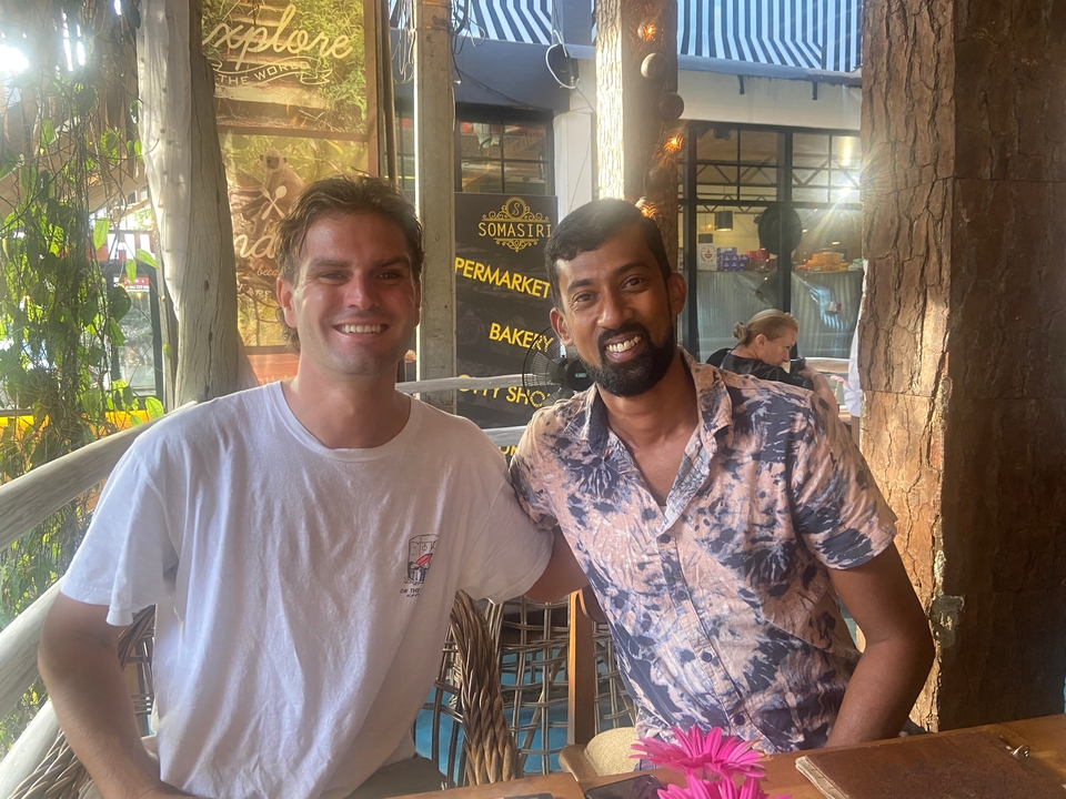 Deux hommes souriants pour une photo dans un café.