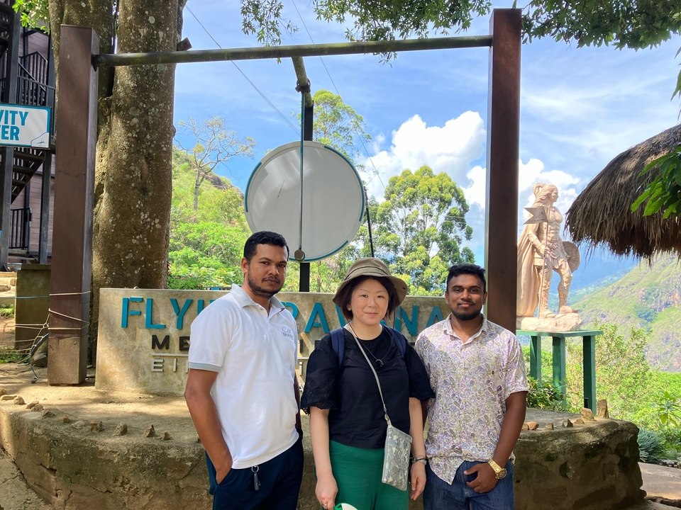 Trois personnes posant près d'un panneau dans un cadre montagneux luxuriant.