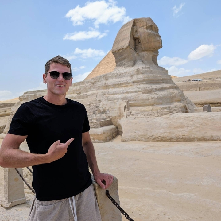 Homme pointant vers le Sphinx avec une pyramide en arrière-plan.
