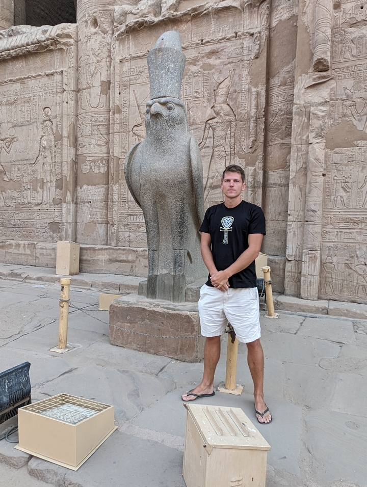 Homme posant devant une statue de l'Égypte antique.