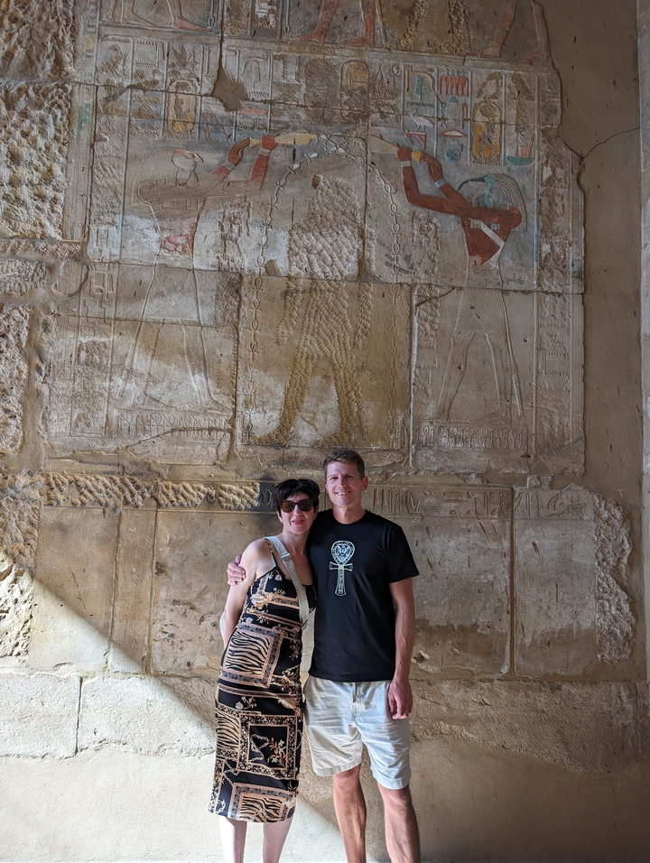 Deux personnes posant devant des sculptures murales de l'Égypte ancienne.