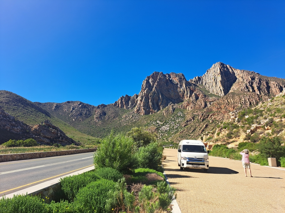 Personne photographiant une chaîne de montagnes au bord d'une route.