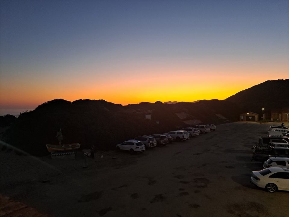 Coucher de soleil sur les collines avec des voitures garées au premier plan.