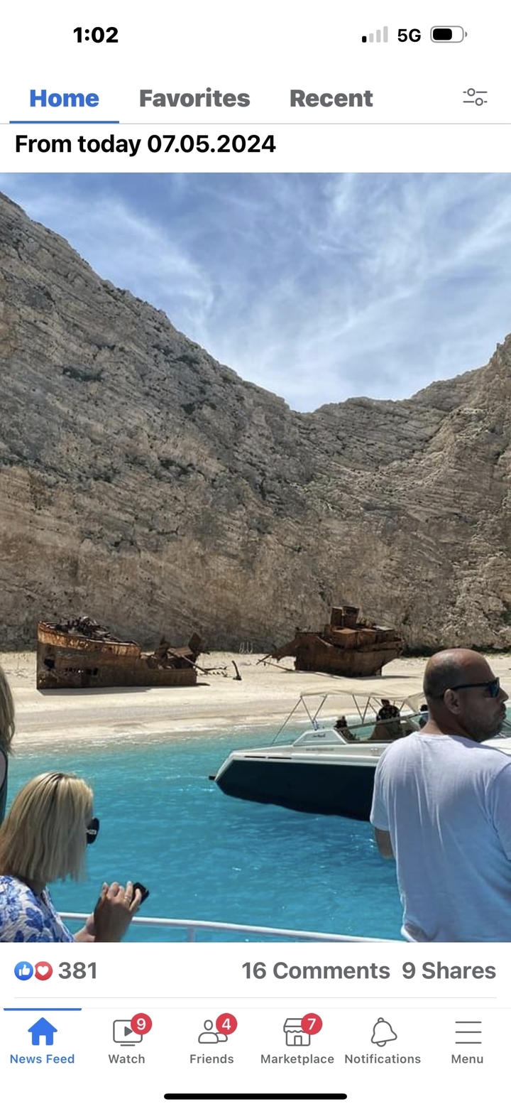Épave rouillée sur une plage de sable avec des falaises abruptes.