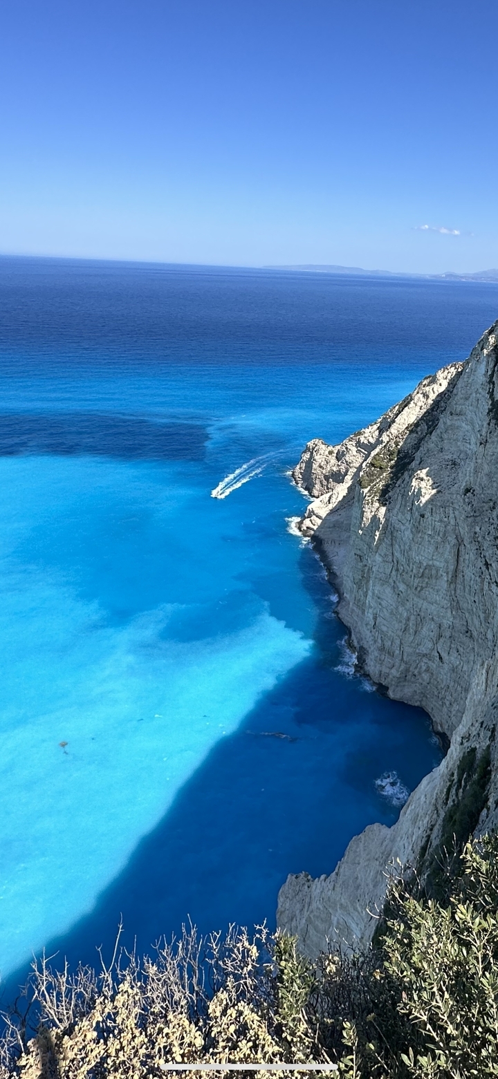 Vue aérienne d'un hors-bord sur une eau bleue éclatante près de falaises abruptes.