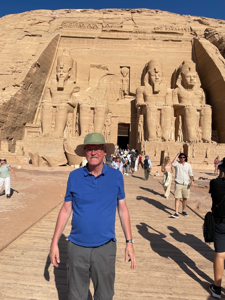 Homme posant devant la façade d'un temple antique avec de nombreux touristes.