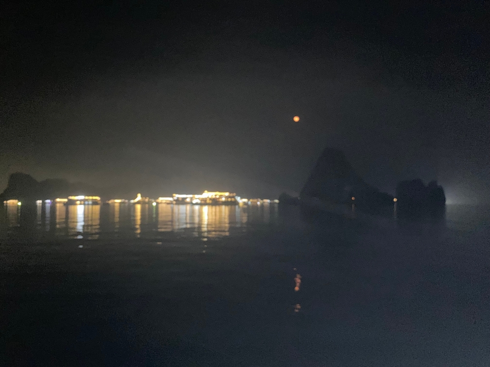 Reflets de navires illuminés sur l'eau la nuit.