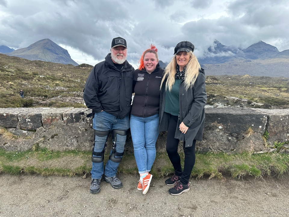 Three people standing together with mountainous scenery.