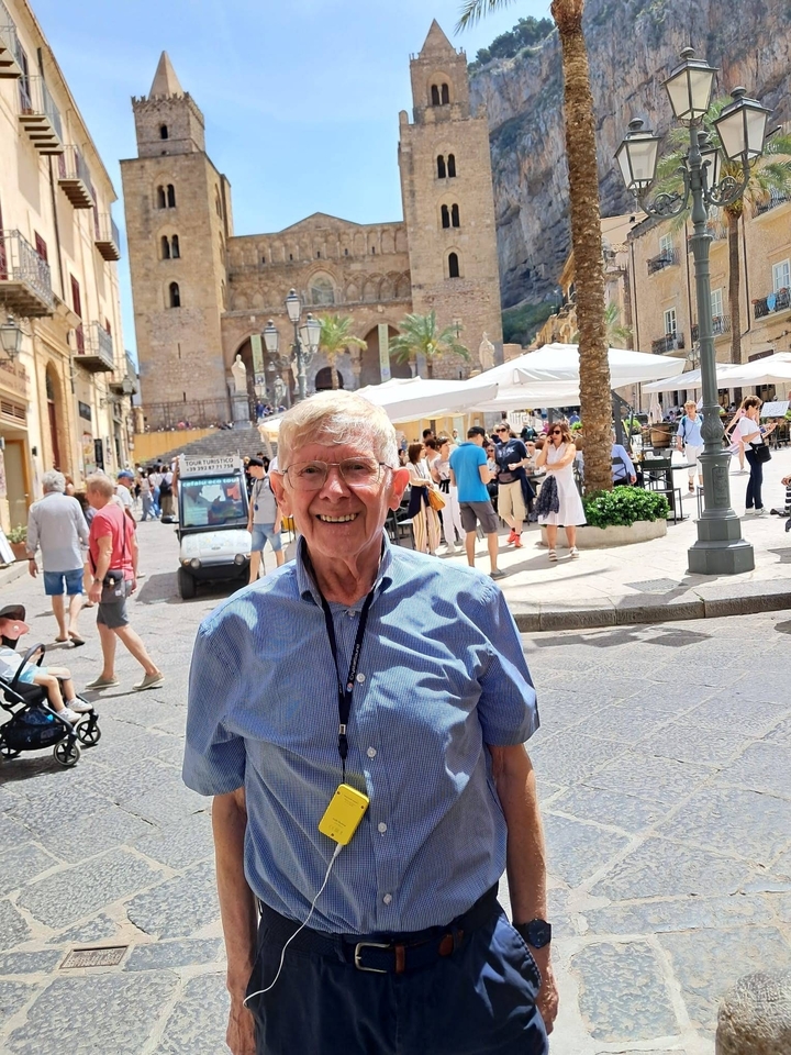 Homme âgé posant sur une place de ville animée.